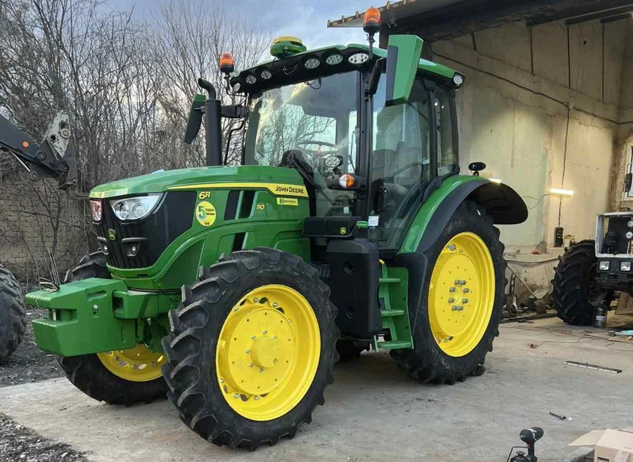 Трактор John Deere с тесни колела и жълти разглобяеми джанти пред стопанска сграда